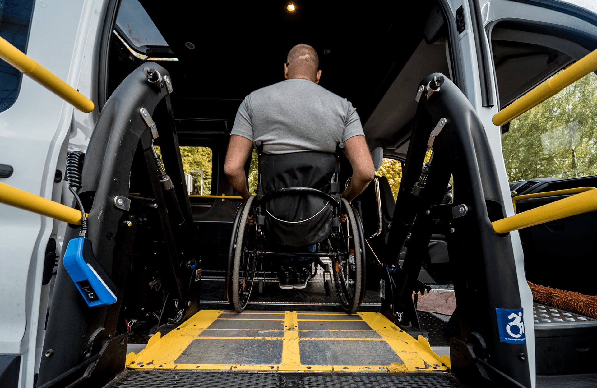 A woman in a wheelchair accessing an equipped wheelchair transport van with the assistance of service personnel